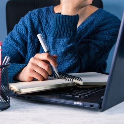 Personne devant un ordinateur en train d'écrire sur son cahier