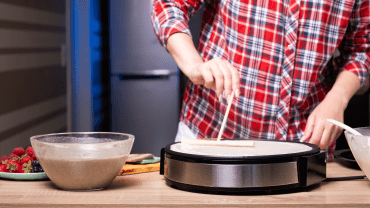 Personne en train de faire une crêpe sur une crêpière professionnelle