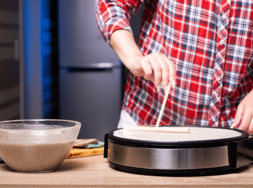 Personne en train de faire une crêpe sur une crêpière professionnelle