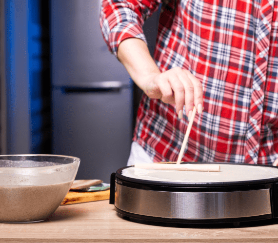 Personne en train de faire une crêpe sur une crêpière professionnelle